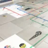 Mactac Permaflex Floorgrip tube-map styled graphic, printed with UV ink, is in the process of being applied to this reception floor area. Some of the prints are already stuck in position while others remain on their white liner waiting to be installed onto the internal ceramic tiles.