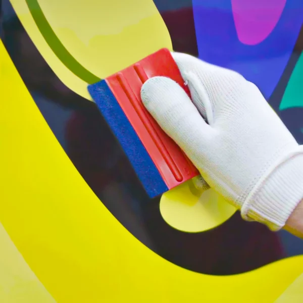 A close-up photo of a felt-edged squeege being used to press the printed conformable wrap vinyl into the contours of the vehicle surface.