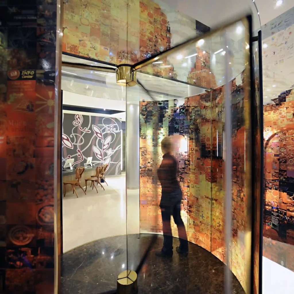 Mactac JT 5000 glass decor vinyls offers a series of print films for self-adhesive window applications and backlit graphics. The image shows a woman entering the lobby of a corporate building through a revolving door with all glass surfaces decorated with a printed abstract design in Autumnal colours.