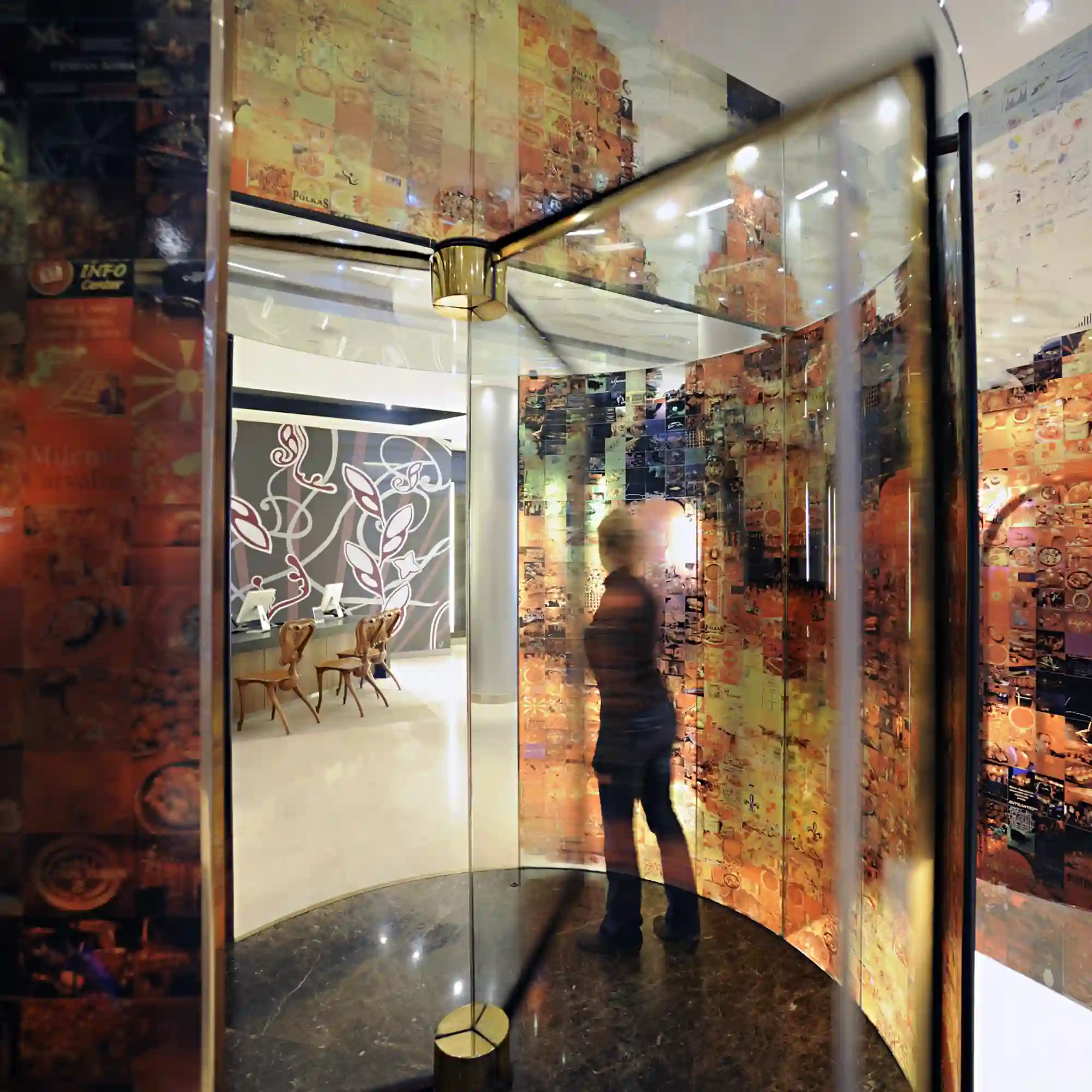 Mactac JT 5000 glass decor vinyls offers a series of print films for self-adhesive window applications and backlit graphics. The image shows a woman entering the lobby of a corporate building through a revolving door with all glass surfaces decorated with a printed abstract design in Autumnal colours.