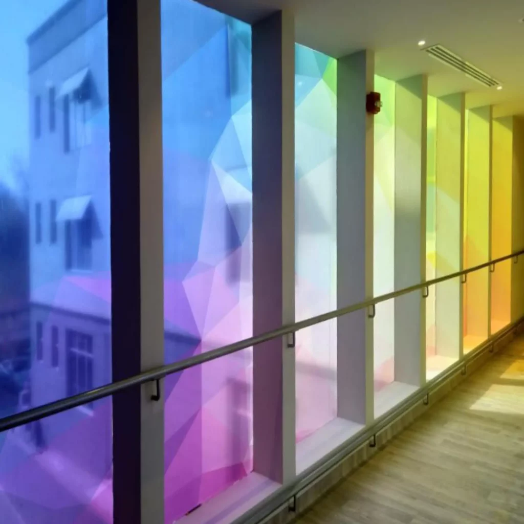 JT 8500 CG-RT, clear gloss transparent print vinyl printed with a colourful, bright geometric abstract design that is applied onto a line of internal corridor windows with the light coming through the window and colouring the room space with all the hues of the printed graphic.