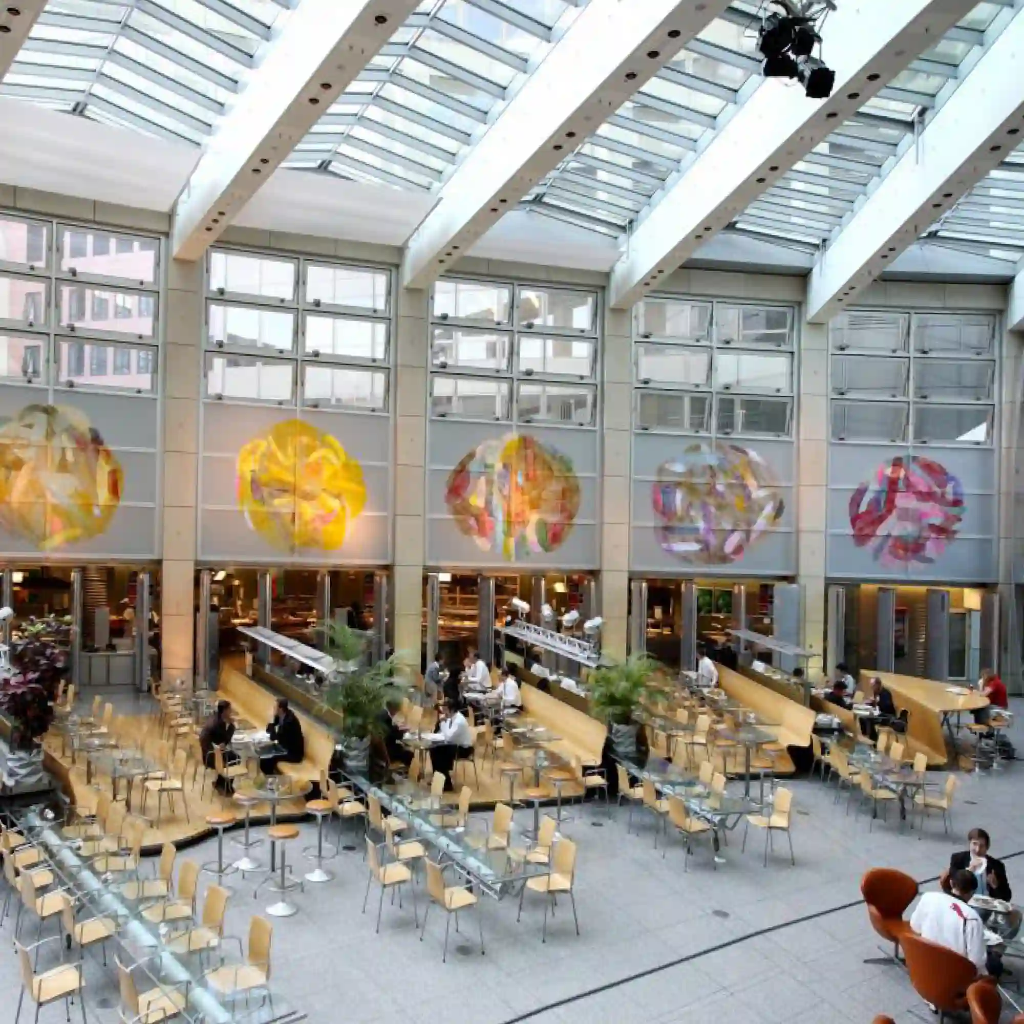 A vibrant glass décor installation featuring Mactac JT8700 CG-RT gloss clear vinyl print graphics. The large restaurant window print decorate a bustling plaza setting, transforming the plaza area with slick, vibrant, modern visual displays, showcasing rich detail.