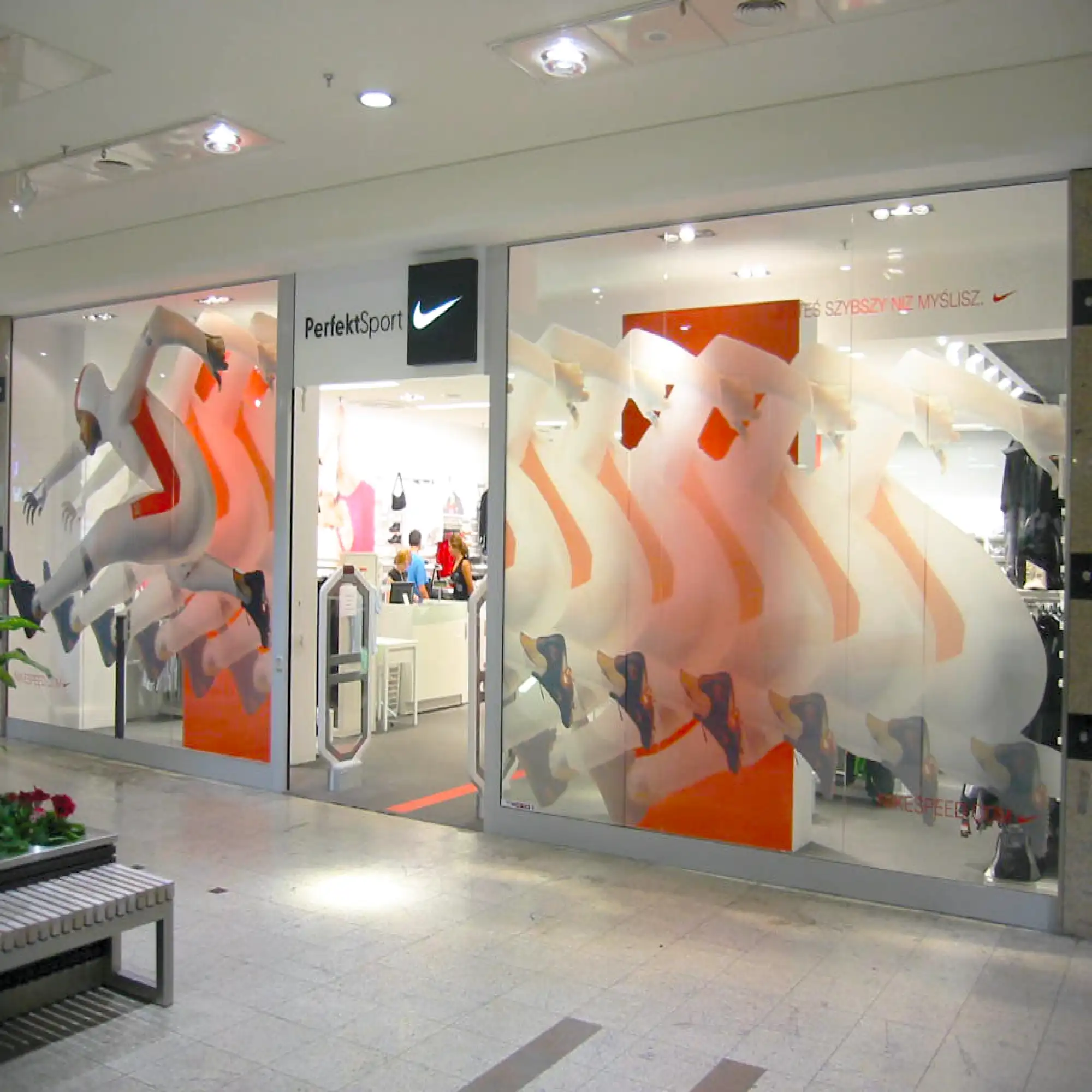 Mactac JT 9700 WT-BFT Frosted effect window print film, with a stylised cut-out graphic of the dynamic movement of an athlete as he hurdles across a large sports retail store front window leaving a dissapearing, feinter trail as he moves from right to left.
