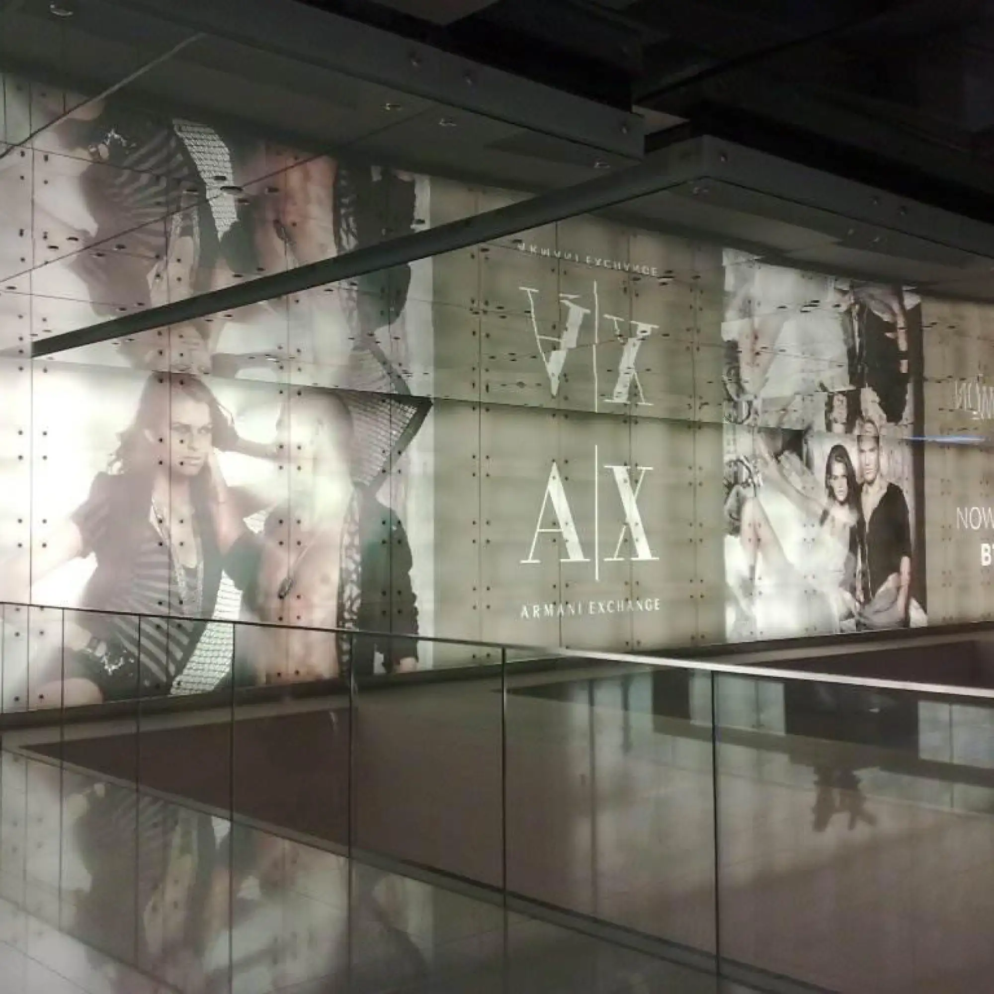 The image features a large format retail display window showcasing a fashion brand retail advertisement which is illuminated by backlighting. The display is printed onto Mactac JT 9700 WT-PT matt white translucent lightbox advertising backlit film enhances the visual impact of the promotions content, providing excellent brightness and clarity as it is lit from behind, making the colours of the advertisement vividly pop, demanding attention and engagement with the display print, making it a prominent feature of the retail space.