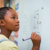 Mactac PG 7034 dry-wipe board film being used to cover a classroom whiteboard and being written on by a young girl doing mathematical sums. This film can also be used as an anti graffiti laminate due to it's similar ink repellent properties where it can be easily cleaned.