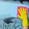 gloss, optically clear anti-graffiti laminate Mactac PG 7036 being wiped clean of spray paint using a suitable cleaning agents with a yellow rubber glove and absorbent cloth, protects the blue graphic print underneath the film and extends the life of the print.