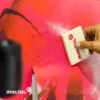 Mactac WW309 gloss print vinyl, printed with a red poppy graphic design, in the process of being applied to a wall using a felt block squeegee, with the release liner folded back aexposing the self-adhesive side of the pinted film as it is pusched to fix in position against the wall.
