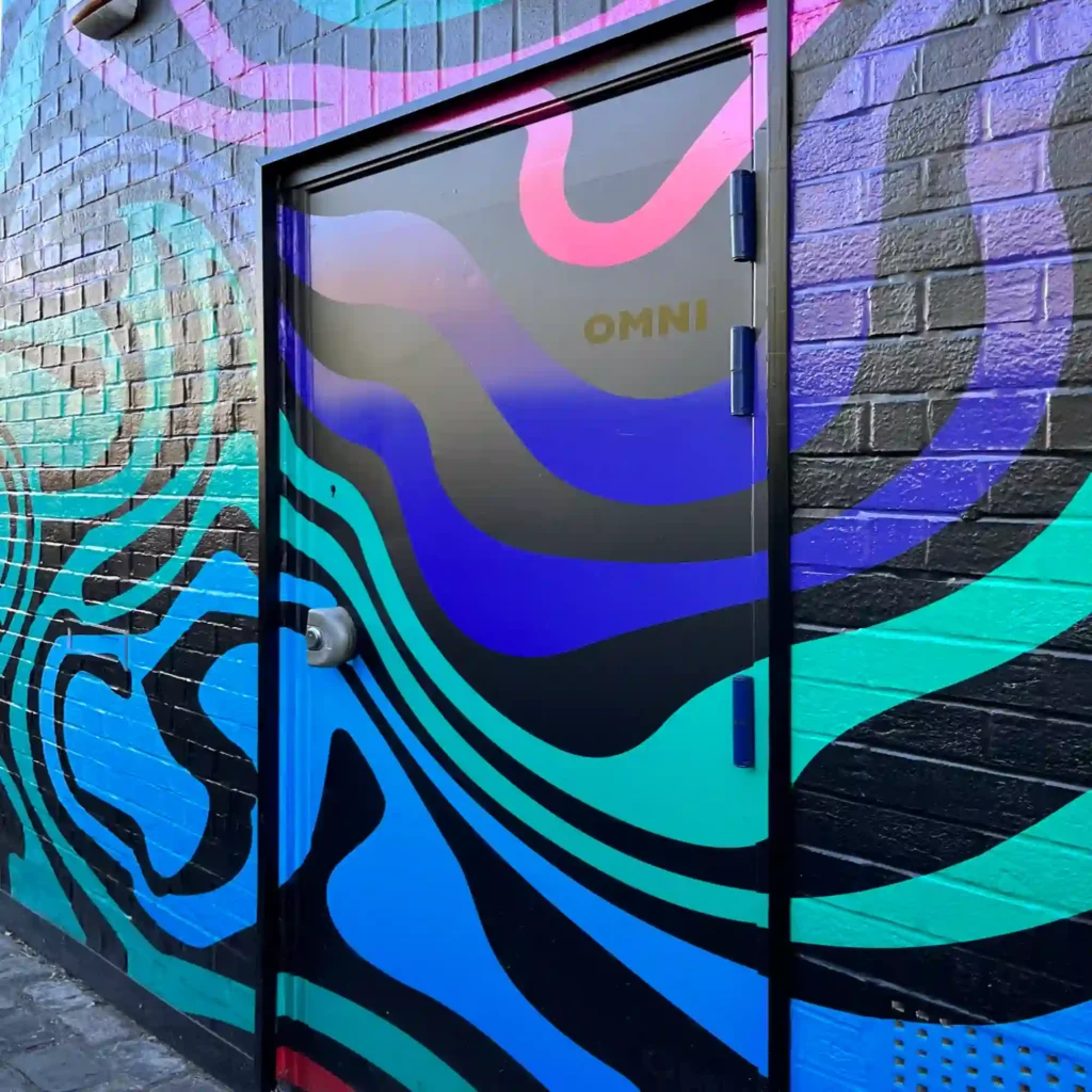 Mactac WW 319 PU Gloss high tack self-adhesive conformable vinyl, printed and applied to an external wall and door wrap with a printed colourful swirl patterned graphic that completely transforms the look of the side of a building.