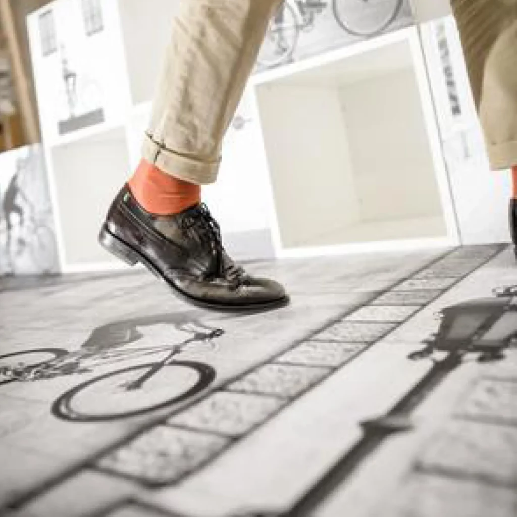 A man walking over Neschen's UV dot print 'n' walk 1part floor graphic film that is printed with images of black and white images of old fashioned style bicycles. Nice orange socks, Sir!