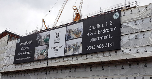 Mesh print banner material wide-format printed sign on the side of an huge construction building site to advertise a new apartment development.