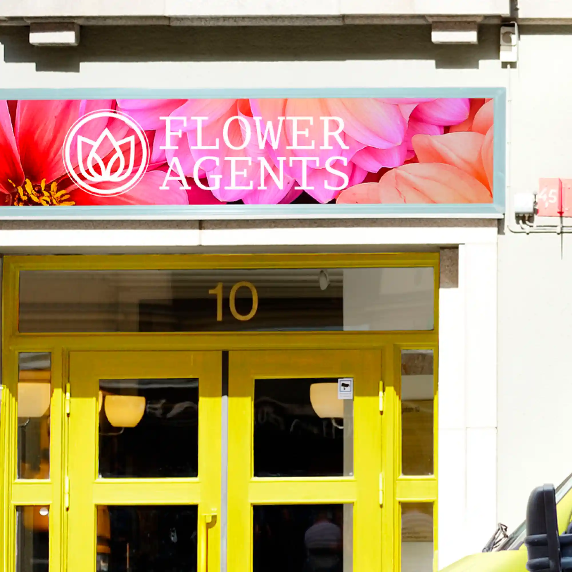 MPI 2004 HOP EA opaque gloss white easy-apply self-adhesive printable graphic vinyl sign film applied to a florists shop front signage, above a yellow front door with bright colourful floral printed imagery incorporating a 'flower agents' company logo.