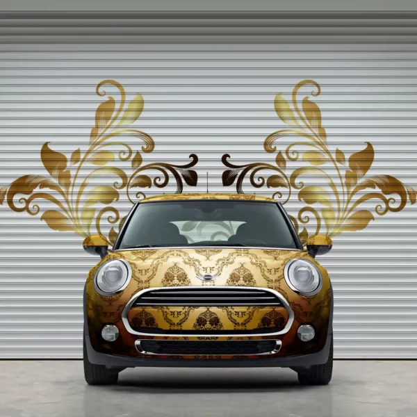 MPI 1104 EA easy to apply, conformable cast print wrapo vinyl print of golden paisly design applied to all the contours of a mini as well as onto the slatted concertina doors behind the vehicle with a printed and cut contour design of some of the pasiley floral design that looks like wings that are protruding from either side of the car.