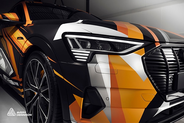 MPI 1105 Speedmaster digital cast wrapping film with best-in-class 3D conformability for the most demanding private vehicle and commercial fleet wraps, sports car wrapped in printed orange and black geometric shapes design.