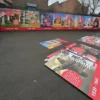 NU-COAT HighGRAB polymeric print films, self-adhesive mounted onto sturdy mounting sheets in the process of being laid out on the floor before being fixed to the exterior fence of a school playground, all the parts being printed with educational display board graphics that depict a historical timeline from the stone age to classical history era.
