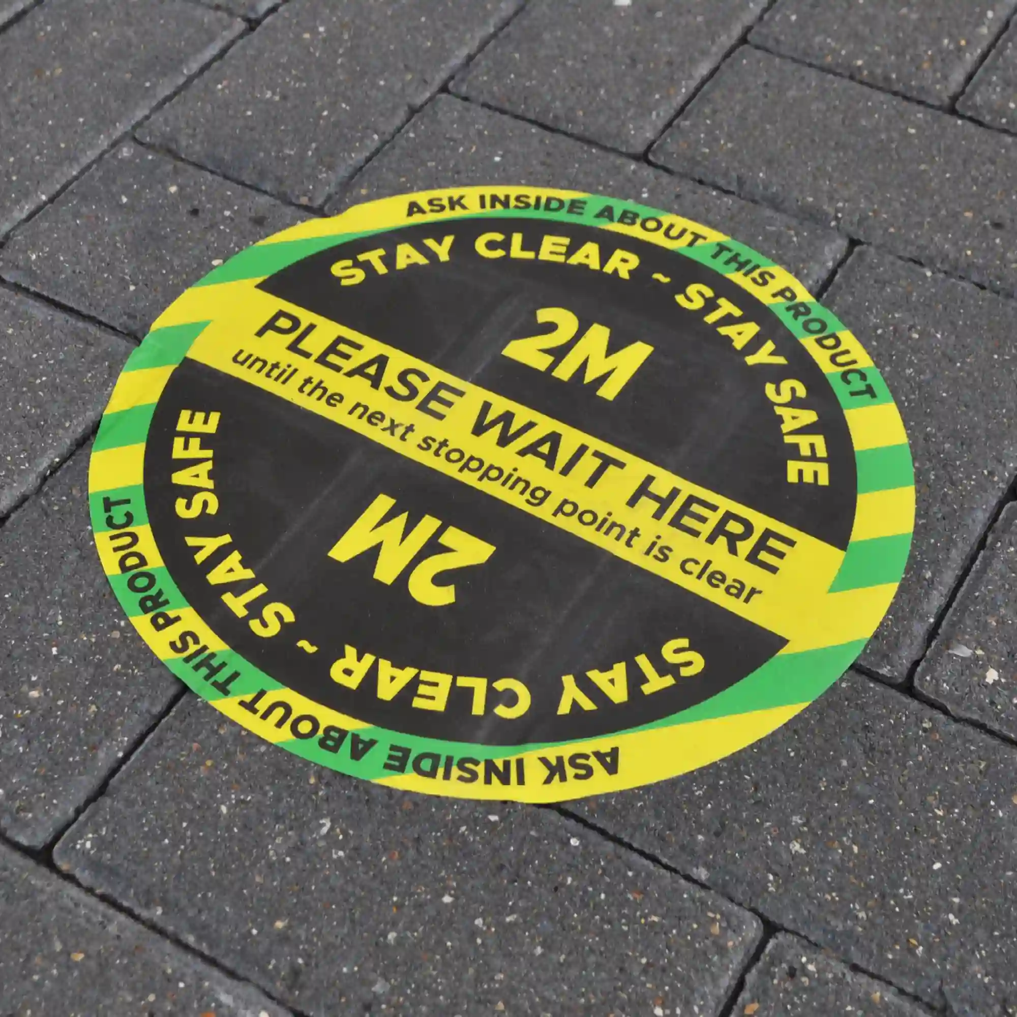 Nu-Coat M15-M with MaxGRAB self-adhesive used for floor graphic applications onto more demanding, rougher flooring surfaces such as the block paving bricks in this picture. A durable social distancing circle is conformed into the exterior paving blocwork with safety and directional messaging.