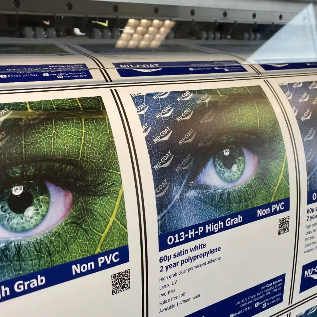 NU-COAT O13-H-P, strong adhesion High Grab PVC-free self-adhesive print film being printed on a wide-format digital printer, with the eco-leafy eye image emphasizing its environmentally friendly, non-PVC composition.
