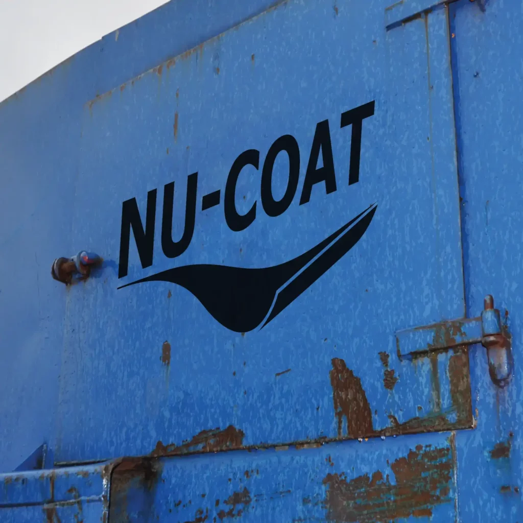 Nu-Sign 'M' Series black self-adhesive sign vinyl has been cut-out and weeded to the shape of the NU-COAT company logo and then stuck onto the door of an outdoor blue skip with rust around some of the edges and is being rained on.