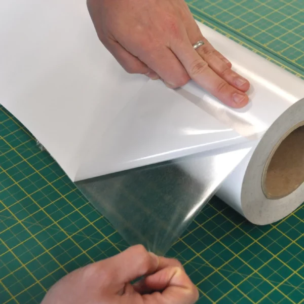 Optically clear mounting film, Filmount Two, FM2, with the corner of the mount film peeled back from the liner exposing the adhesive side and revealing the transparent adhesive film.