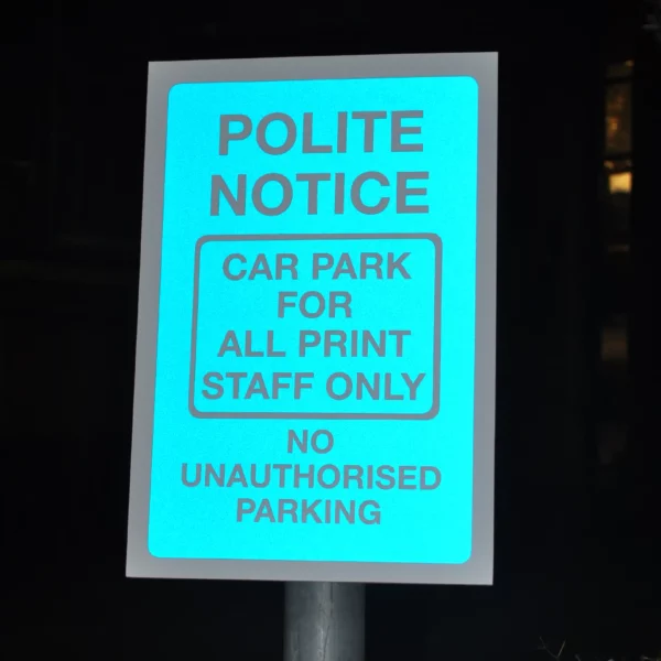 ORALITE 5400-050 Blue reflective sign vinyl as the background of a 'no unauthorised parking' cut-vinyl sign with the blue film brightly reflecting the camera flash out of the dark night.