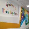NU-COAT P12-H-K HighGRAB self-adhesive polymeric graphics vinyl with a kraft release liner, printed with bright colourful graphics to create a bespoke wall covering which also includes plotter cut-out printed text that says "welcome to the main outpatients" area.