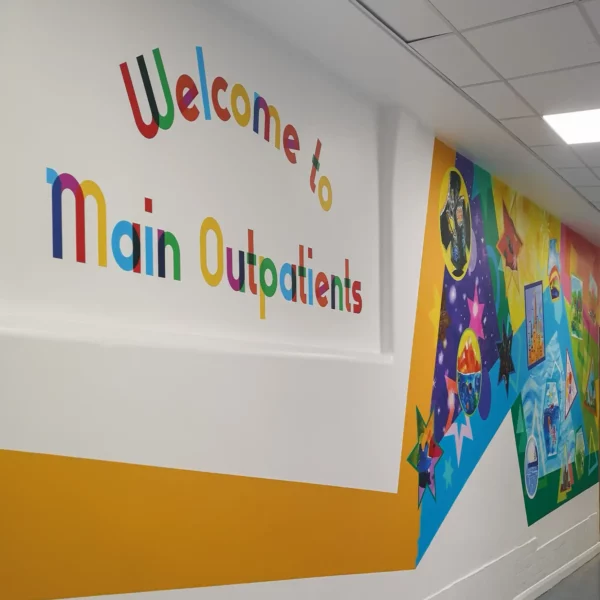 NU-COAT P12-H-K HighGRAB self-adhesive polymeric graphics vinyl with a kraft release liner, printed with bright colourful graphics to create a bespoke wall covering which also includes plotter cut-out printed text that says "welcome to the main outpatients" area.