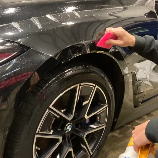 Paint Protection Film in the process of being squeegeed into the surface of a vehicle wheel arch panel and the wet application solution being removed so it sticks and stays in position on the vehicle.