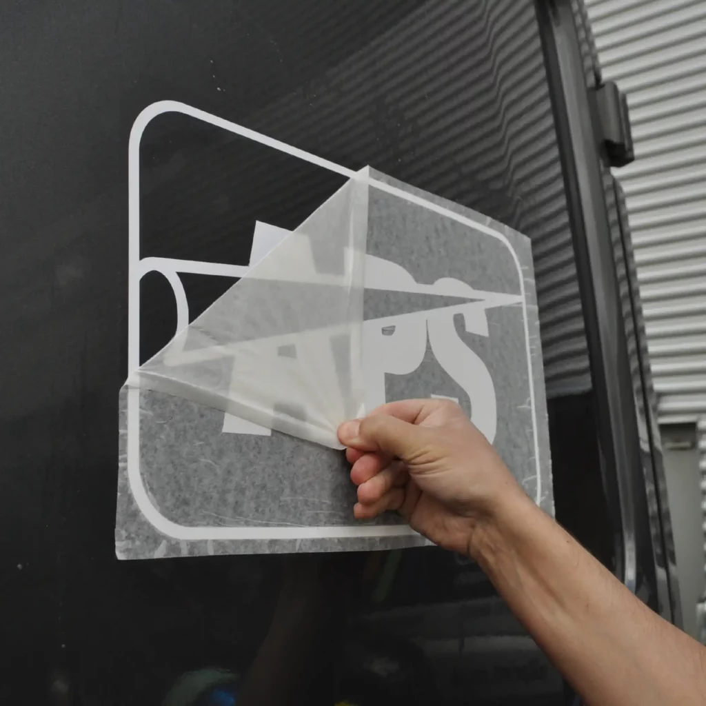 Peeling away RTape 4075 RLA application tape after the cutout van logo vinyl graphic and transfer paper have been wet applied to the side of the van. When the wet application method is used with this application paper it allows for easier final positioning and ease of removal of the transferring tape without disturbing the vinyl image.