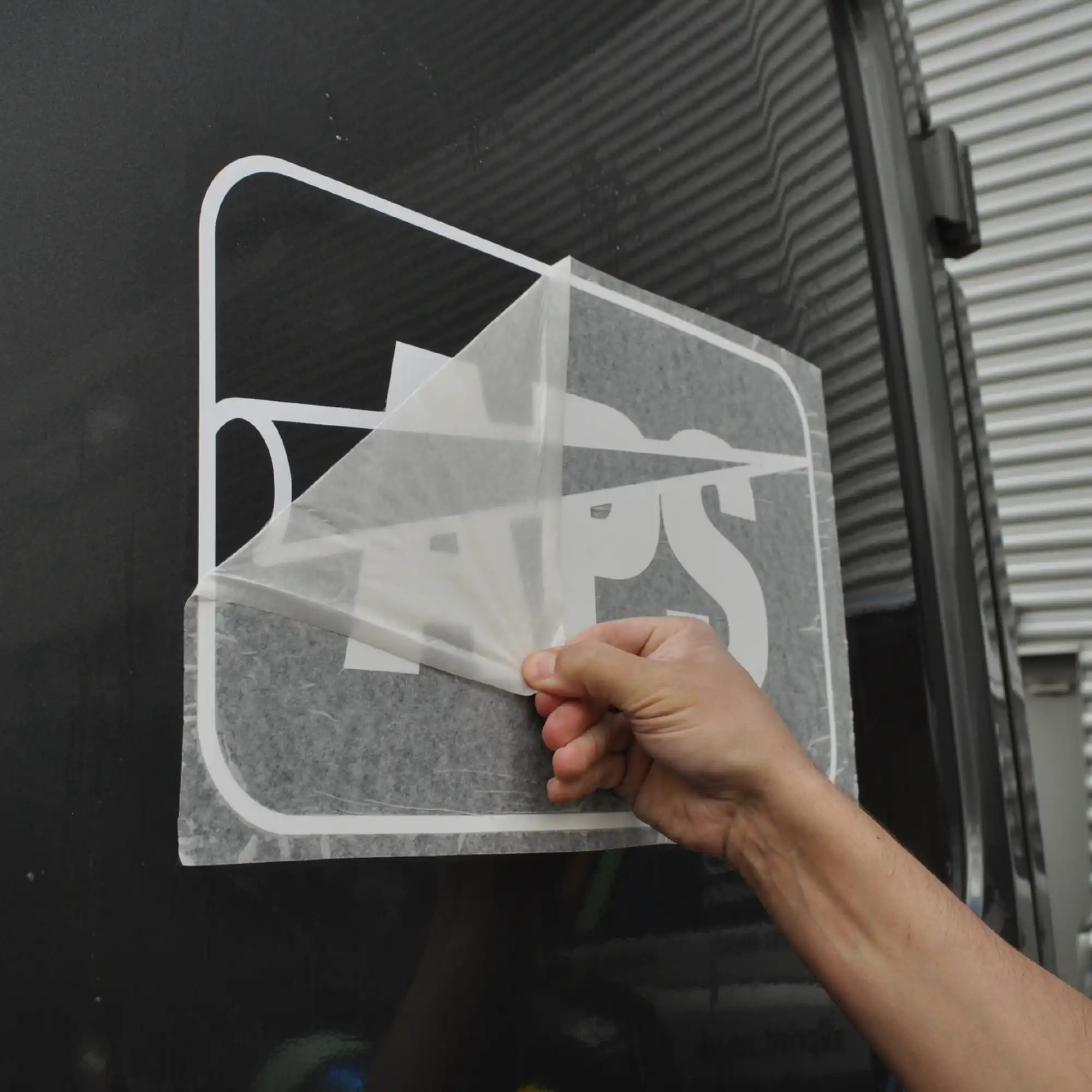 Peeling away RTape 4075 RLA application tape after the cutout van logo vinyl graphic and transfer paper have been wet applied to the side of the van. When the wet application method is used with this application paper it allows for easier final positioning and ease of removal of the transferring tape without disturbing the vinyl image.