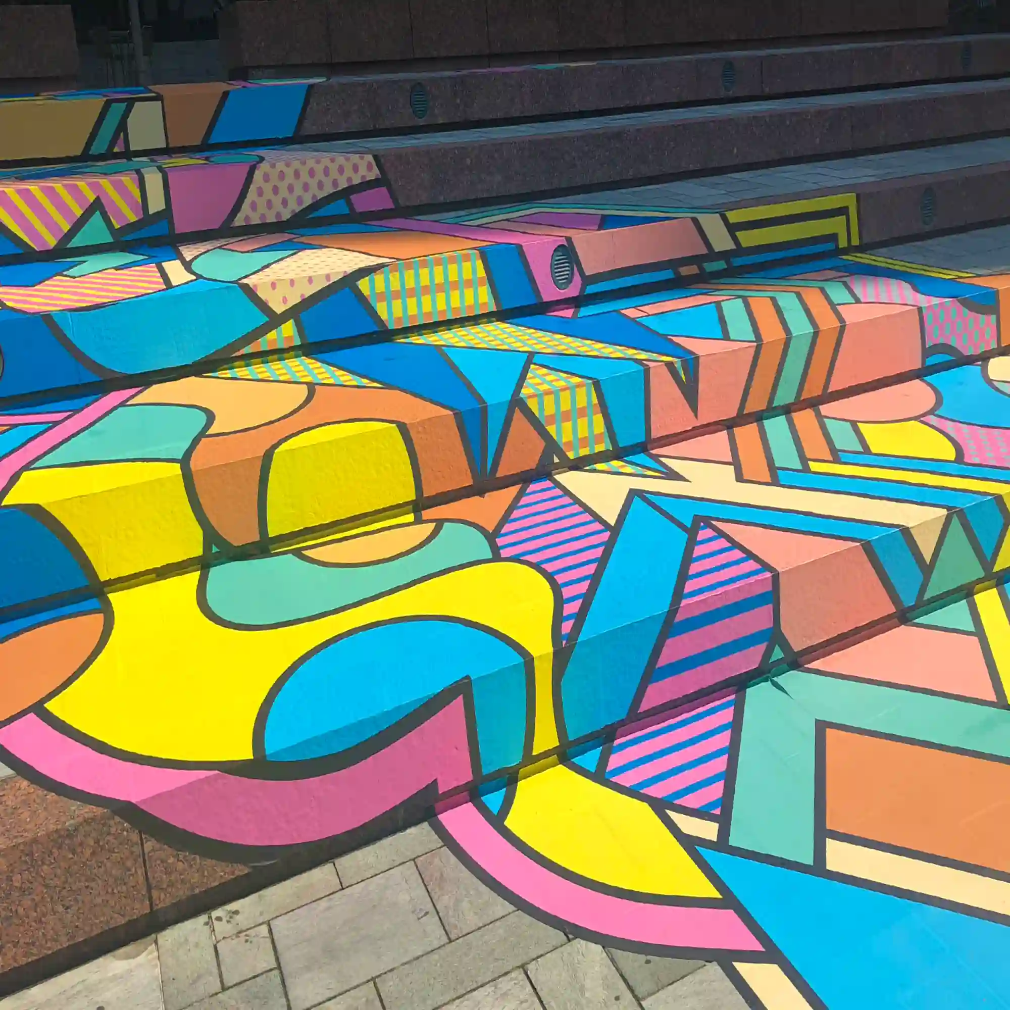 Mactac Streetrap printed floor graphic vinyl laminated with StreetLAM matched slip-rated laminate covering deep steps at an outside venue to decorate the flooring surfaces with bright, vibrant colours and a geometric inspired art design.