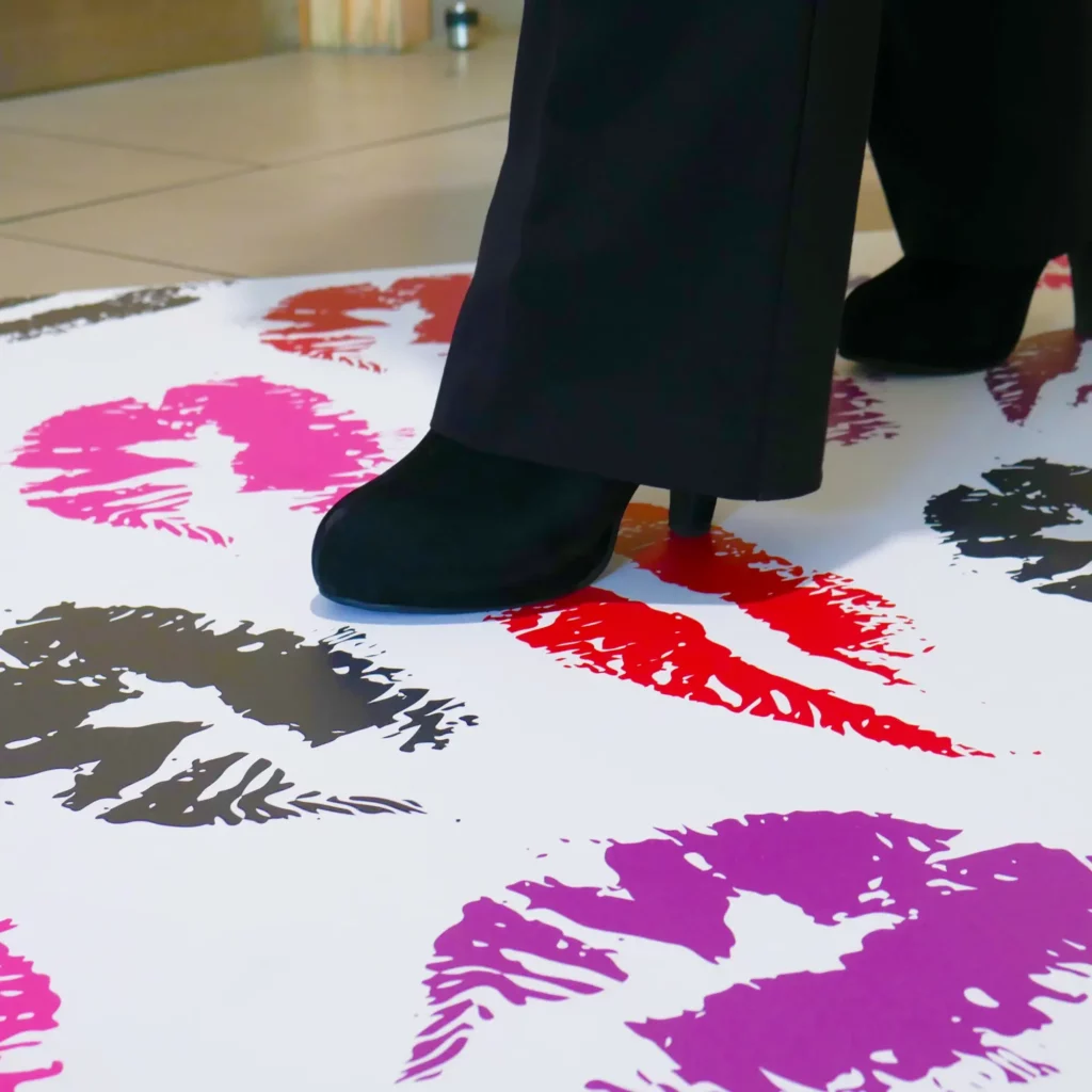 JT 8300 WM-RT Dot Floors printed with a lipstick kiss design in bright pinks, reds and other brighth shades is situated on a lobby floor and can be seen being walked over by a lady wearing high heeled shoes.