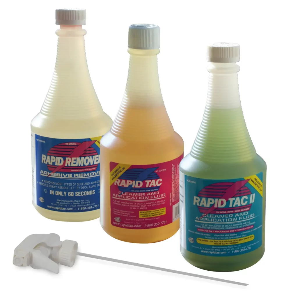 A group photo of the 3 x application fluids from RAPIDTAC; 1x adhesive remover and 2 x sign application fluids. From left to right: pale lemon coloured RAPIDTAC Adhesive Remover fluid, pink coloured RAPIDTAC Original sign vinyl application fluid and RAPIDTAC II light green coloured application fluid with the screw on/off white sprayer nozzle laid out in front for inserting into each of the bottle types.