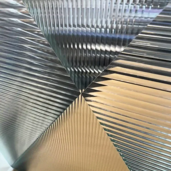 Reeded Glass window films provide decorative privacy to glass surfaces, with a subtle lens effect the clear stripes are available in two widths which are pictured here applied to a large glass partition wall where the 2 different lens sizes have been cut into symetrical triangle pieces and re-assembled to form an "X" shape with the slimmer RG6 pattern film positioned vertically and the wider RG12 lens width applied horizontally, both meeting at a point in the middle of the film. The obscurity of the films are apparent as the photo looks through the films and the view behind is obscured as it is broken up into sections where the light is bent giving a shallow ribbed effect.