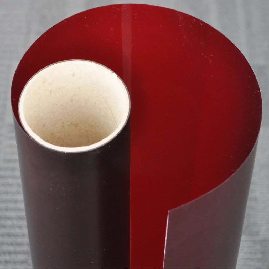 Ruby stencil film, un-used on its wide format roll with the film and release liner slightly unfurled to show the translucent red colour of the vinyl as light comes through.