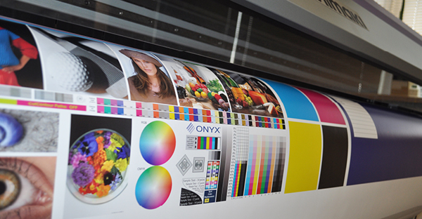 SIHL 3683 TriSOLV Primeart Blueback SA 210 billboard poster printing paper is shown with the roll media threaded through a wide format inkjet printer and vibrant colourful graphics being printed onto this opaque, cover-all white paper.