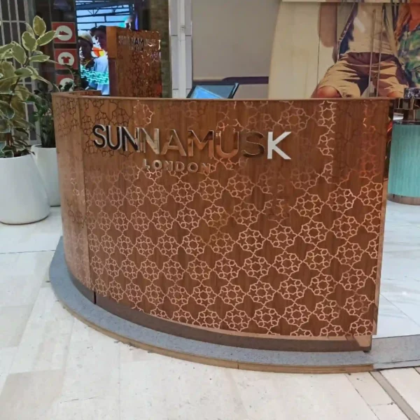 T72-P Rose Gold metallised graphics film applied to the outside of a reception desk in a geometrically styled, flower patterned cut-vinyl graphic that provides a delicate reflective colour to the decoration of the curved wooden facade of the counter area and also on the complimentary background plynths.