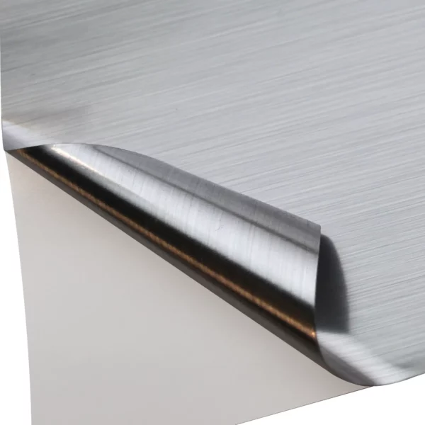 NU-COAT T80-P Brushed One-Way Silver self-adhesive film with the corner of the vinyl peeled back to reveal both sides of the film - the face side has a full brushed metal effect while the reverse (adhesive side) has a less visible brush effect, so when applied to a window the same finish would not be viewable from both sides of the glass.