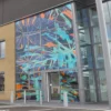 Crystal clear window graphic printed on TSTC8 non-adhesive print film designed fo rsuperb image clarity and a sleek, seamless finish on glass surfaces. The photo shows a full glass building-front covered with a bright abstract jungle leaf/camouflage style design.