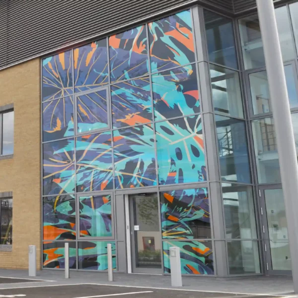 Crystal clear window graphic printed on TSTC8 non-adhesive print film designed fo rsuperb image clarity and a sleek, seamless finish on glass surfaces. The photo shows a full glass building-front covered with a bright abstract jungle leaf/camouflage style design.