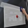 TT60 application tape holding a fairly intricate cut-vinyl logo graphic together on the back door of a van while the vinyl is fixed into permanent position with a squeege before final removal that will leave the completed vinyl sign behind.
