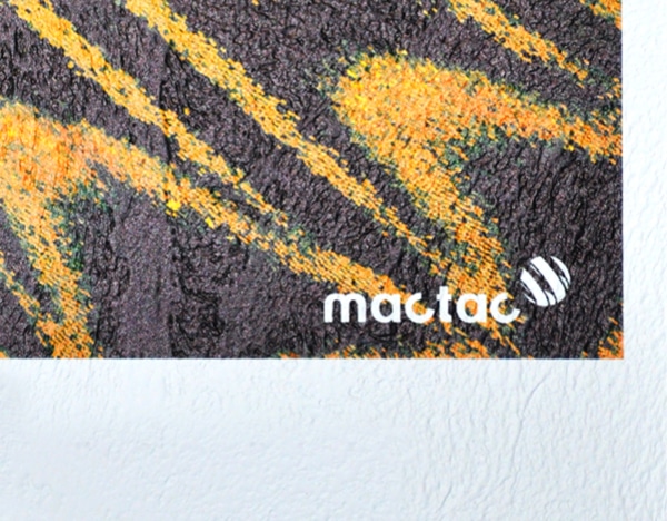 WW Veneziano satin white self-adhesive textured wall wrap vinyl is shown in close up detailing the printed and unprinted areas of a sample of the material with the heavily embossed stucco pattern of this print media. The printed part of the sample shows the product brand group image of a deep yellow orange and black butterfly wing with the Mactac brand logo in the bottom right corner. At the very bottom of the image you can see the pattern of the unprinted satin white base material.
