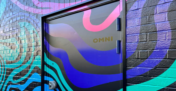 WW 319 PU gloss white printed PVC-free self-adhesive graphic film applied onto an external textured brick wall and smooth flat door in a vibrant coloured swirling line patterns on a dark background.